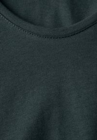 Tummanvihreä puuvillakangas, jossa on sileä pinta, pyöreä kaula-aukko ja hienovarainen tikkaus reunoilla.