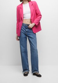 Světlý růžový blazer se strukturálními rameny, bílý krátký top, modré džíny s vysokým pasem a černé ploché boty. Jednoduchý, ležérní outfit.