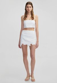 Top corto blanco combinado con una mini falda blanca que presenta un patrón floral y un dobladillo con forma de ola. Tejido suave con una apariencia texturizada.