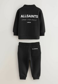 Melna kokvilnas sporta krekla un bikses komplekts. Iekļauj baltu "ALLSAINTS" logo un tekstu aizmugurē un kabatā, ribotās aproces un elastīgu jostasvietu.