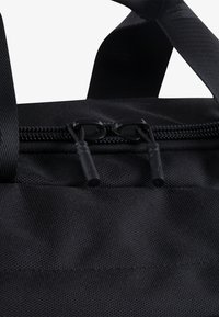 Primer plano de una bolsa de tela negra que presenta una apertura con cremallera y tiradores texturizados, mostrando un diseño compacto y duradero.