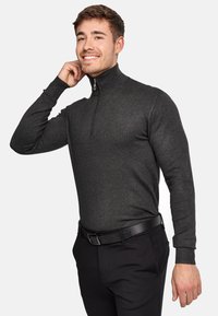Mørkegrå lynlås sweatshirt med høj krave og lange ærmer, båret med sorte bukser og et matchende bælte. Glat tekstur.