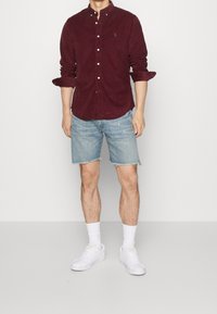 Vínová košile na knoflíky, džínové šortky, bílé tenisky. Košile má límec, šortky mají třepený lem. Jednoduchý, ležérní design.