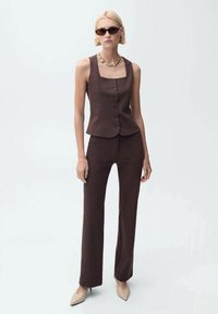 Gilet marron ajusté avec un col carré et cinq boutons, associé à un pantalon droit assorti et des escarpins beiges à bout pointu.