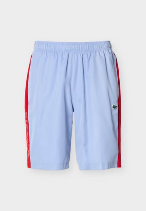Light blue athletic shorts with elastic waist, red side panels, white "LACOSTE" text on left leg, and a green crocodile logo on right leg.