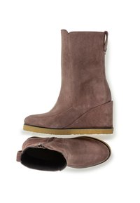 Botas de cuña de ante marrón con un acabado suave, punta redondeada, cremallera lateral y suela de goma para mayor tracción. Cuenta con una pestaña para ponerlas y quitarlas fácilmente.