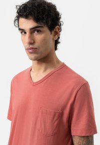 Korte mouwen, v-hals t-shirt in koraal, met een kleine borstzak, gemaakt van zachte stof met een gladde textuur.