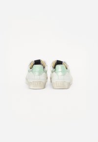 Sneakers bianchi con un accento in verde menta testurizzato e un tirante nero, caratterizzati da una suola spessa e la scritta "1973" impressa sul tallone.