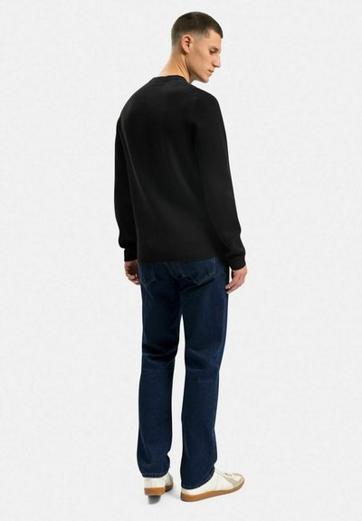 Sort strikket sweater med lange ærmer, parret med mørkeblå denim jeans og hvide sneakers, set fra ryggen.