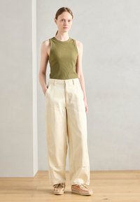 Débardeur côtelé vert olive, pantalon large crème avec poches avant, et baskets texturées multicolores ; design minimaliste.