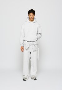 Hellgrauer Kapuzenpullover mit einer Fronttasche, kombiniert mit weit geschnittenen Sweatpants. Lockere Passform, weicher Stoff, mit betontem Bündchen.