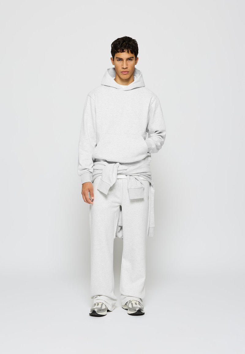 Sweatshirt à capuche gris clair avec une poche avant, associé à un pantalon de survêtement à jambes larges. Coupe décontractée, texture douce, avec un accent de taille à nouer.