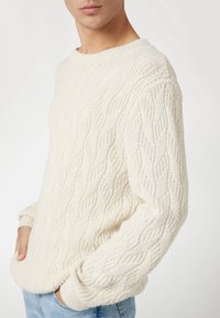 Maglione a coste color crema con scollo rotondo, maniche lunghe e un motivo testurizzato. Vestibilità casual, materiale morbido e polsini a coste.