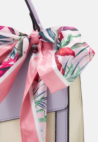 Handtas van lichtpaarse textuur. Voorzien van een satijnen strik in het roze met een bloemenpatroon, wat het gestructureerde ontwerp accentueert.