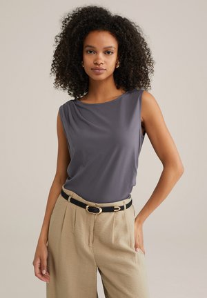 Sleeveless grey top with a boat neckline, made of soft fabric. Styled with high-waisted beige trousers and a black belt with a gold buckle.