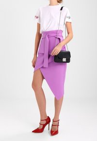 Vit t-shirt med blomsterbroderi, kombinerad med en lila asymmetrisk kjol och röda högklackade skor. Accessoarerna inkluderar en svart handväska.