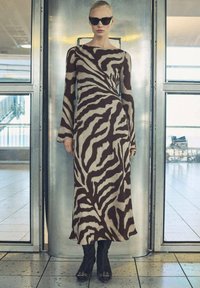 Maxi dress in beige with dark brown zebra stripes, long sleeves, and a boat neckline; paired with knee-high black boots.