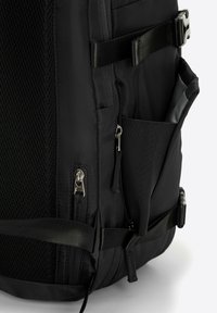 Zaino nero con un pannello in rete testurizzata, tasche con zip, spallacci regolabili e tessuto resistente. Presenta una tasca laterale in rete per ulteriore spazio di archiviazione.
