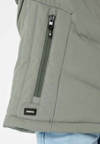Giacca isolante grigia con tasca con zip, texture trapuntata e etichetta con marchio sull'orlo.
