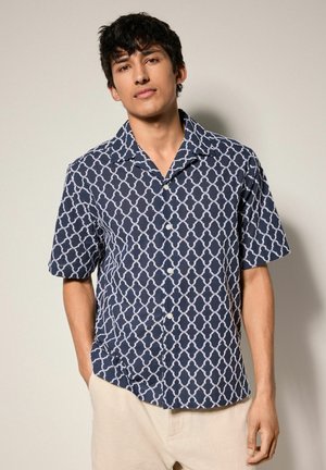 Camicia a maniche corte con bottoni di colore blu navy e un motivo geometrico bianco, con colletto aperto e una trama di tessuto liscia.