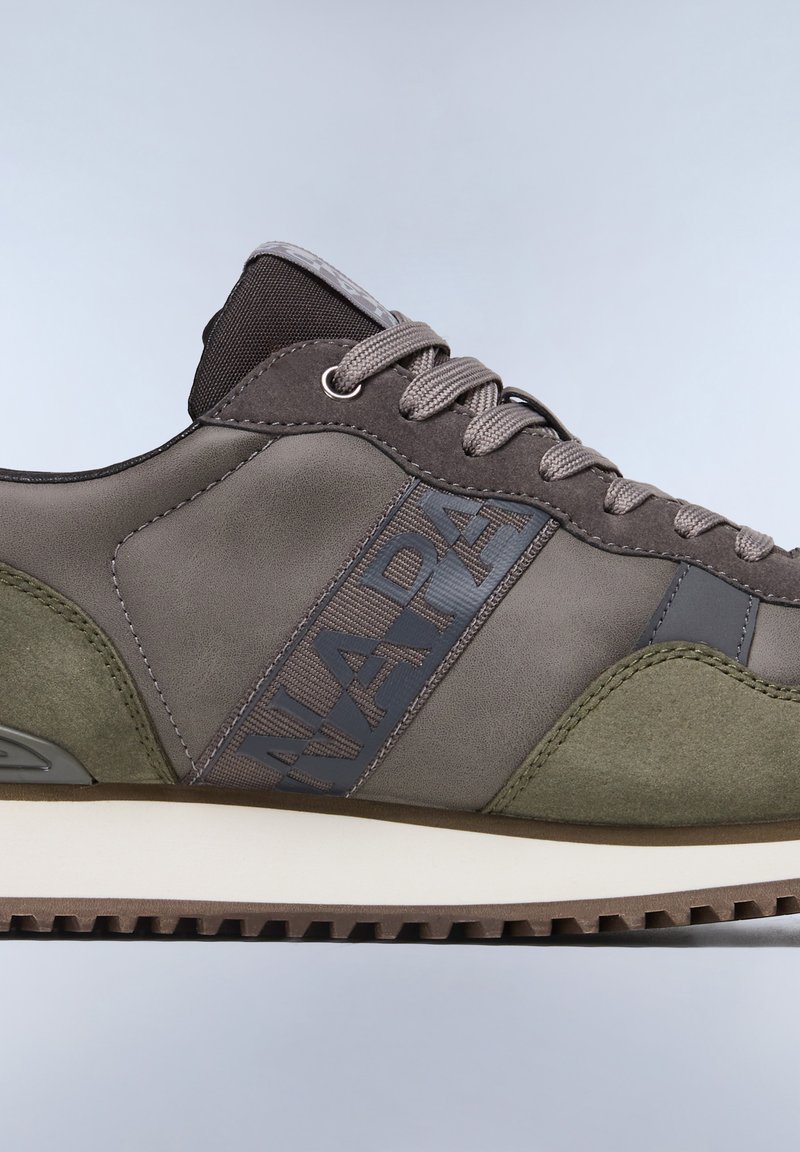 Zapatilla en gris verde con materiales de ante y cuero suave. Presenta cordones grises y una banda con logotipo, acentos texturizados y una suela blanca.