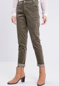 Olijfgroene corduroy broek met een slim-fit ontwerp, voorzien van een gestikte textuur en omgeslagen pijpen. Gecombineerd met beige enkellaarsjes.