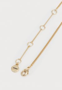 Gouden ketting met een combinatie van schakels en cirkelvormige accenten; beschikt over een DKNY-label en een kreeftsluiting.