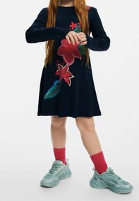 Laivastonsininen mekko, jossa on pitkät hihat ja punaisen sekä vihreän sävyistä kukkaistikkausta. Yhdistetty vaaleansinisiin tennareihin ja vaaleanpunaisiin resorillisiin sukkiin.