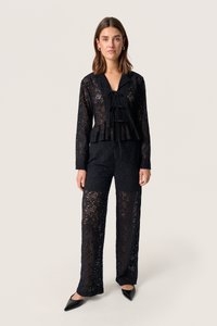 Musthave mustrõngaga must pitsist pluus ja püksikomplekt, millel on peplum vöökoht, V-kujuline kaelus nööri detailiga ja pikad varrukad. Viimistletud terava musta jalatsiga.