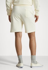 Ljust gula bomullsshorts med en bakficka, i kombination med grå ribbade strumpor och vita skor, visade från baksidan.