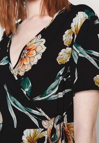 Musta kukkaroitu mekko, jossa on suuria kerma- ja oransseja kukkia, vihreitä lehtiä sekä lyhyet hihat, joissa on sidontatyyli vyötäröllä.