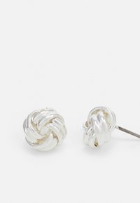 Cercei cu studs în formă de nod argintii, având un design răsucit cu textură netedă și finisaj lucios. Fiecare cerceadă are un suport cu tijă pentru o purtare sigură.