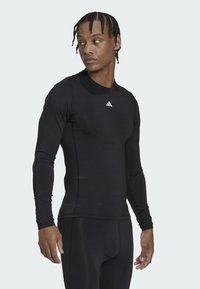 Svart langermet treningsskjorte laget av elastisk materiale med rund hals, med en hvit Adidas-logo på brystet.