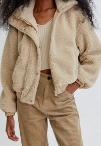 Beige fleece jacket with a textured exterior, zip front, and elastic cuffs. Paired with corduroy pants in a matching tan color.