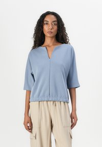 Top curto de manga curta azul claro com decote em V e bainha franzida, feito de tecido suave, exibido com calças cargo bege.