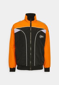 Black and orange jacket with a high collar, contrasting white piping, and a logo on the left chest. Texture is smooth with elastic cuffs.