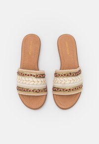 Platta slip-on sandaler med en beige konstlädersula. Ovandelen har vävda vita och flerfärgade dekorativa band. Ingen klack.
