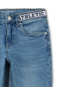 Jeans de mezclilla en azul claro con un corte regular; presentan una cinturilla en blanco y negro con la inscripción "ATHLETIC", botón de metal y diseño clásico de cinco bolsillos.