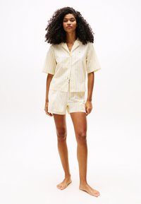 Ensemble de pyjama à rayures jaunes et blanches avec manches courtes et shorts. Fabriqué en tissu léger. Comprend un col et une fermeture à boutons devant.