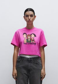 T-shirt cropped rosa con grafica raffigurante tre personaggi dei cartoni animati e la scritta "Cynicism degli anni '90". Realizzata in cotone, maniche corte, vestibilità rilassata.