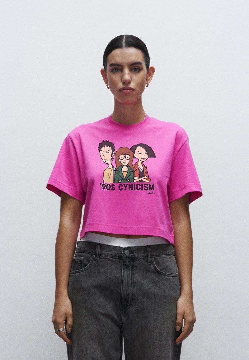 T-shirt cropped rosa con grafica raffigurante tre personaggi dei cartoni animati e la scritta "Cynicism degli anni '90". Realizzata in cotone, maniche corte, vestibilità rilassata.