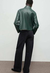 Chaqueta de cuero verde recortada con cuello de muesca, combinada con vaqueros de denim oscuros de pierna ancha. Textura suave y diseño minimalista.