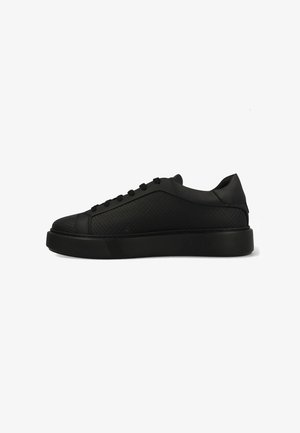 Zapatilla negra con lados texturizados, punta redondeada, suela negra sólida y seis ojales para los cordones. Diseño minimalista sin marcas visibles.