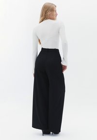 Zwarte wijde broekspijpen met een hoge taille, met een gladde textuur en riemlussen, gecombineerd met een aansluitend wit long-sleeve top.