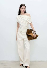 Krema off-shoulder majica z nabranim detajlom, v kombinaciji s širokimi bež hlačami in rjavim suedenim toaletnim torbicam, ki ima kontrastno naramnico.