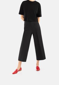 T-shirt noir court, pantalon large taille haute noir, et mocassins rouges brillants à petit talon. Design minimaliste, textures lisses.