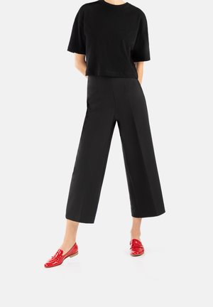 Schwarzes, kurzes T-Shirt, hochgeschnittene schwarze weit geschnittene Hose und glänzende rote Slipper mit niedrigem Keilabsatz. Minimalistisches Design, glatte Texturen.