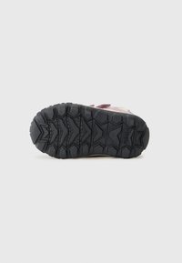 Suela de goma negra con un patrón texturizado en zigzag para un mejor agarre, que presenta un logo y pequeños orificios de drenaje para la transpirabilidad.