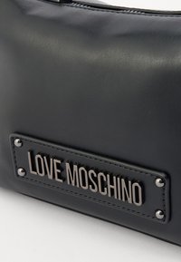 Black faux leather bag featuring a stitched logo patch with silver hardware and studs, highlighting a smooth texture and sleek design.