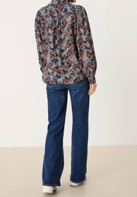 Blusa floreale blu scuro, con motivi rossi e verdi, maniche lunghe a sbuffo e dettaglio arricciato sul retro, abbinata a jeans blu scuro.